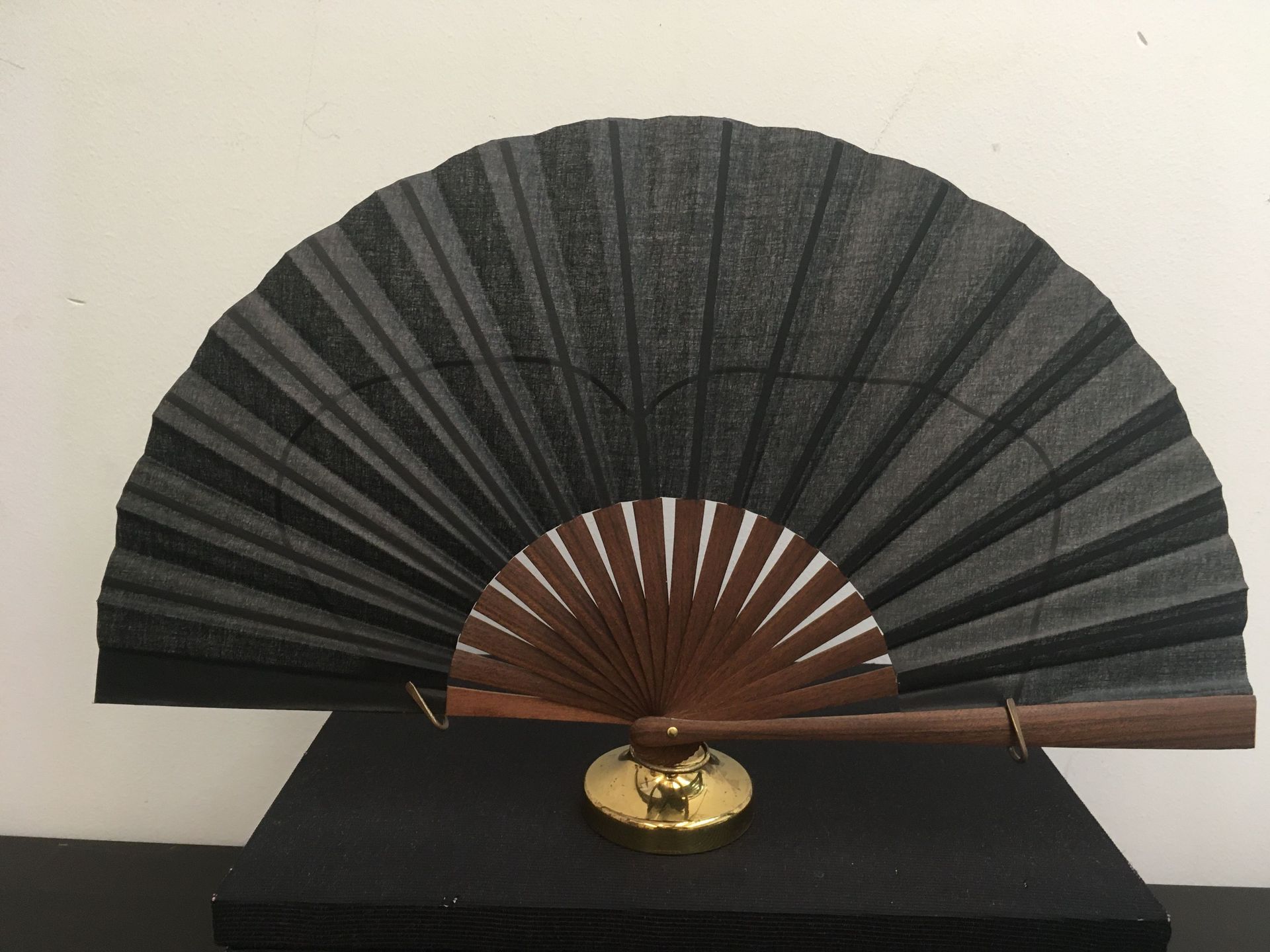 Un abanico negro con mango de madera está sobre una mesa negra.