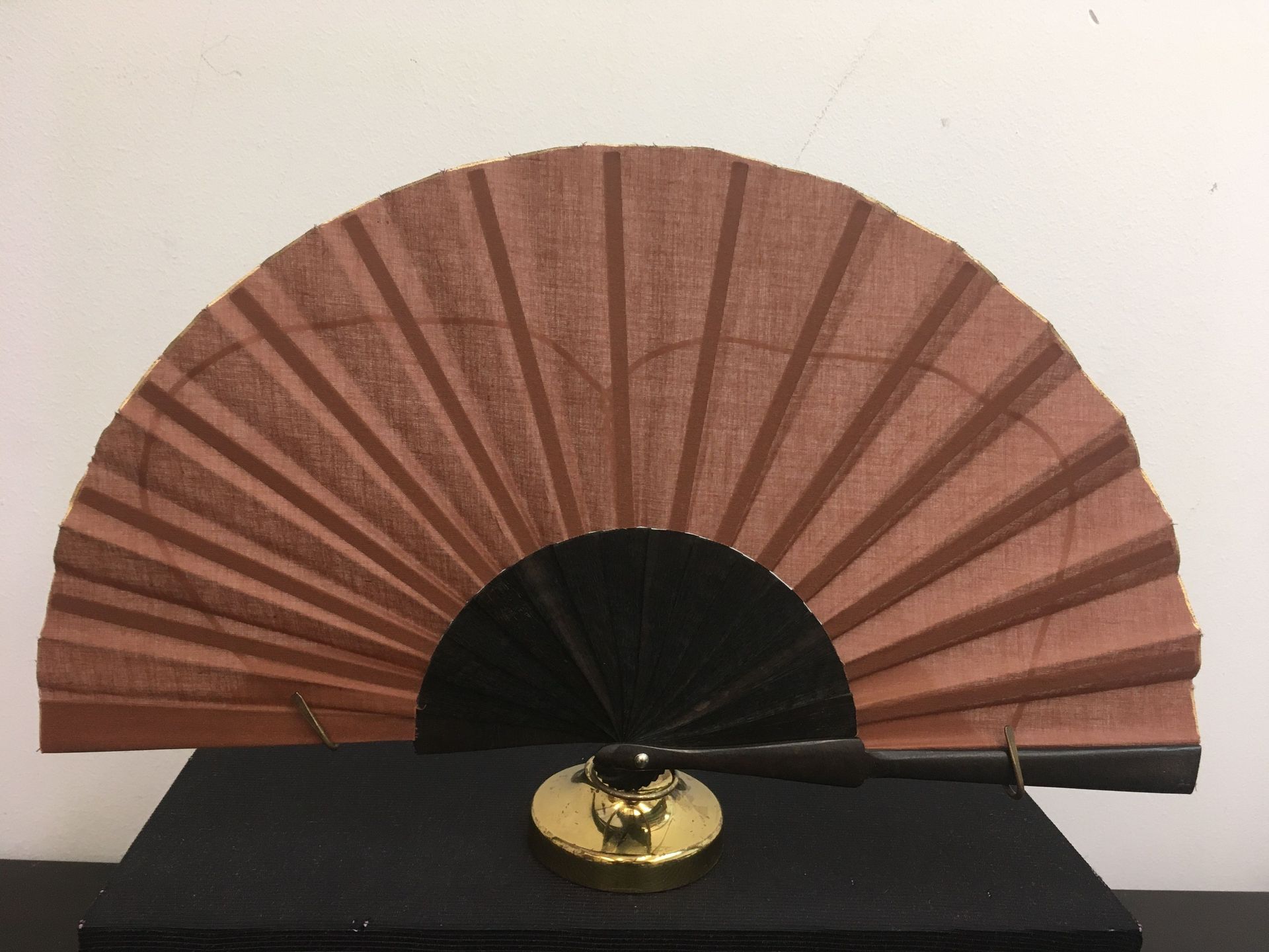 Un abanico marrón con un mango negro está sobre una mesa negra.