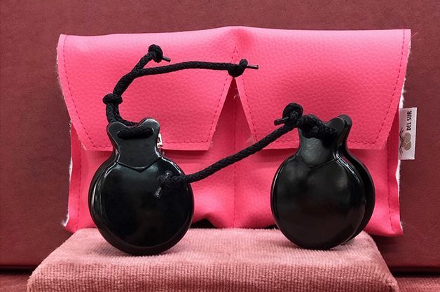Un par de castañuelas negras colocadas encima de una almohada rosa.
