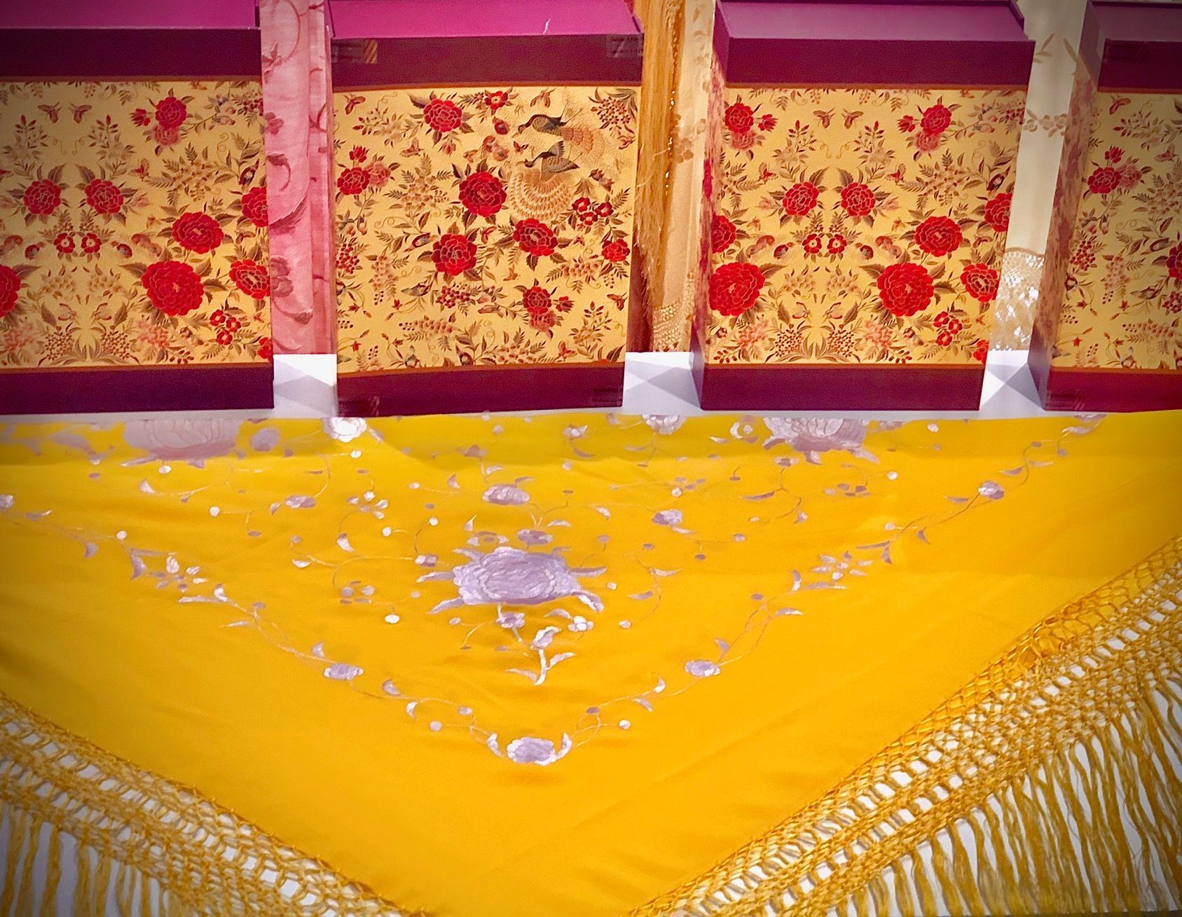 Un paño amarillo con flecos reposa sobre una mesa junto a cajas con flores.