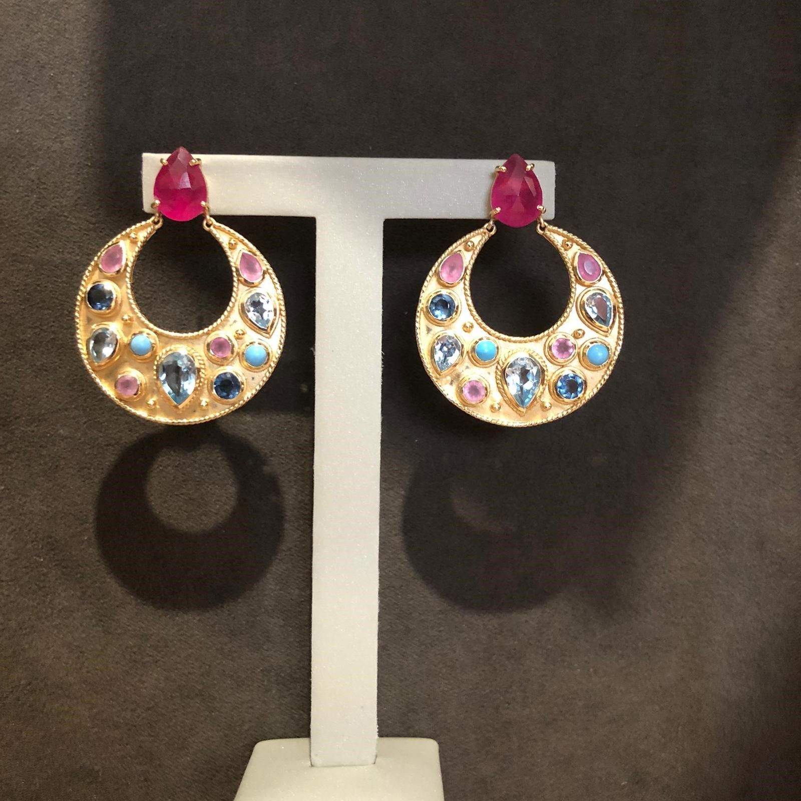 Un par de pendientes de aro dorados con piedras rosas y azules.
