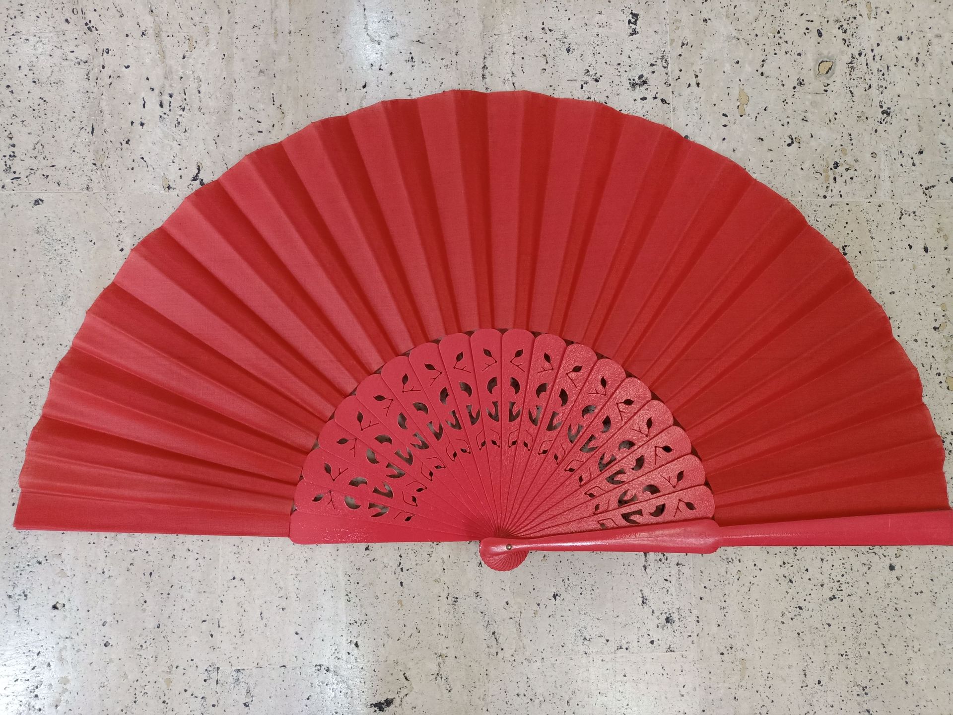 Un abanico rojo está sentado sobre una superficie blanca.