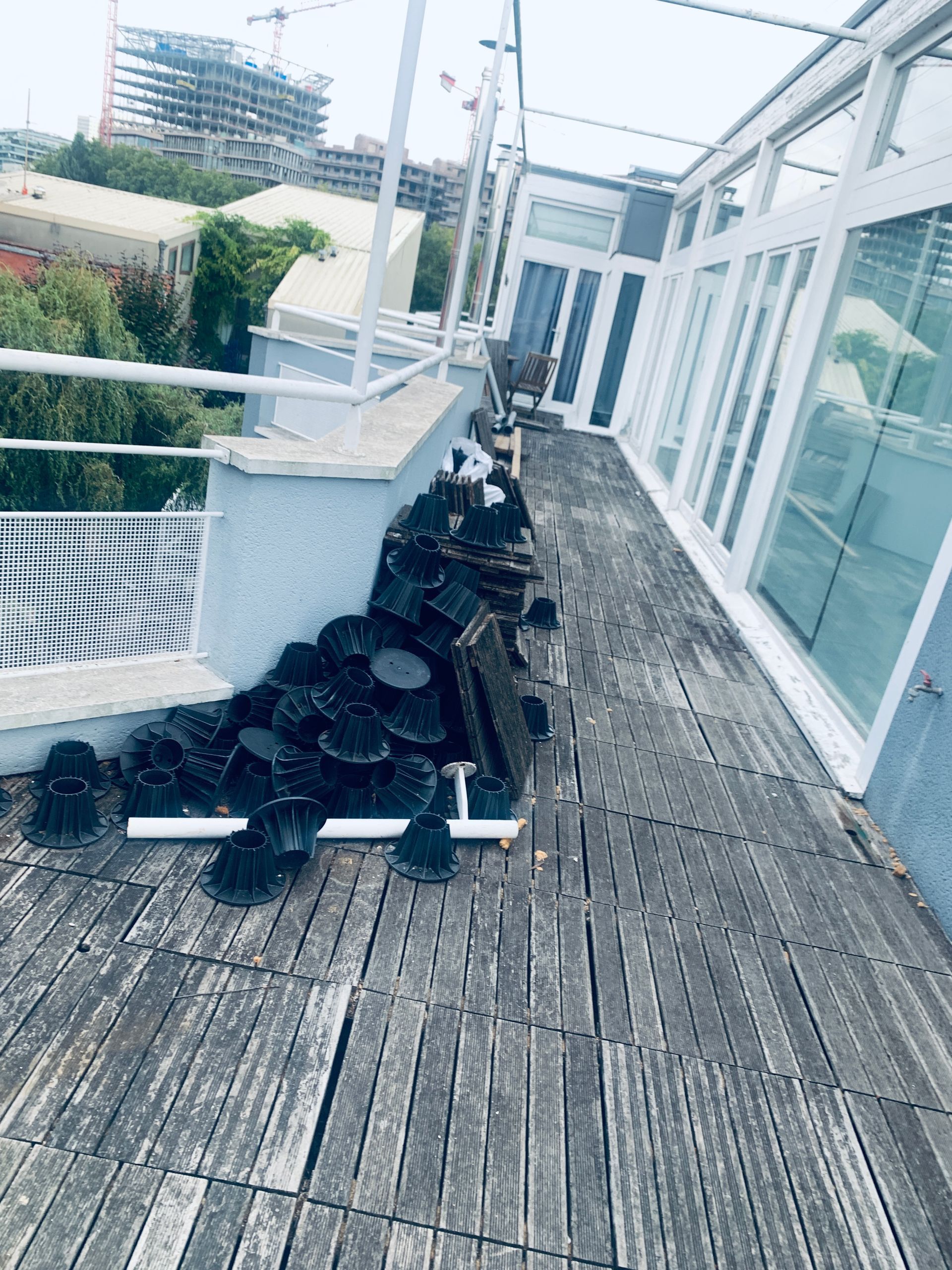 Toit-terrasse avec parquet patiné. Objets noirs empilés le long d'un mur, à côté de fenêtres à cadre blanc.