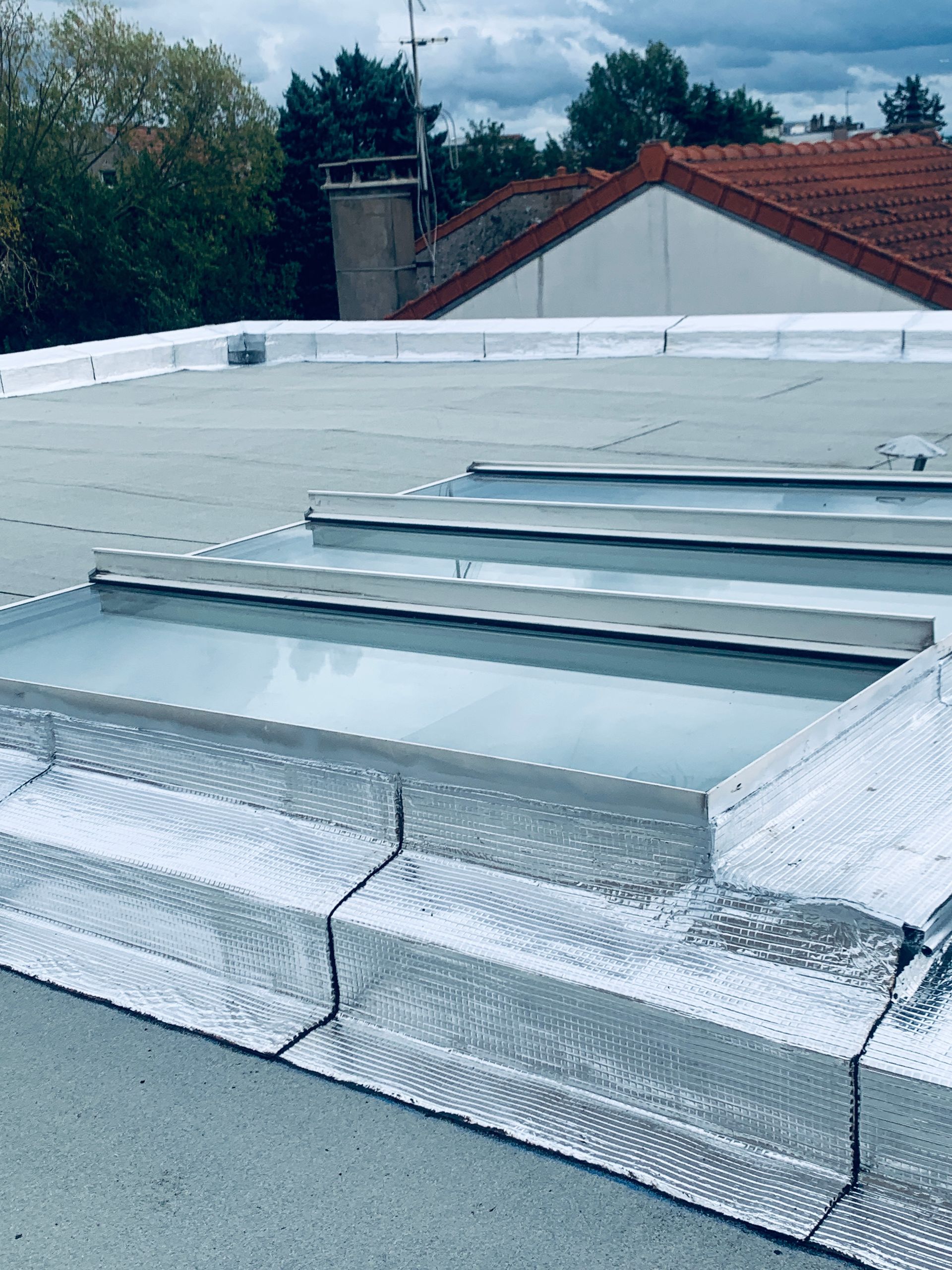 Toit plat avec solins argentés autour des puits de lumière.