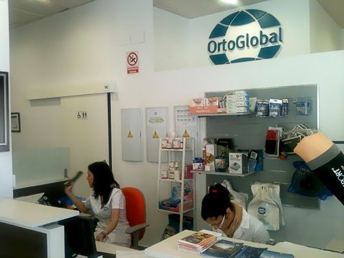 Una mujer está sentada en un escritorio frente a un cartel que dice ortoglobal