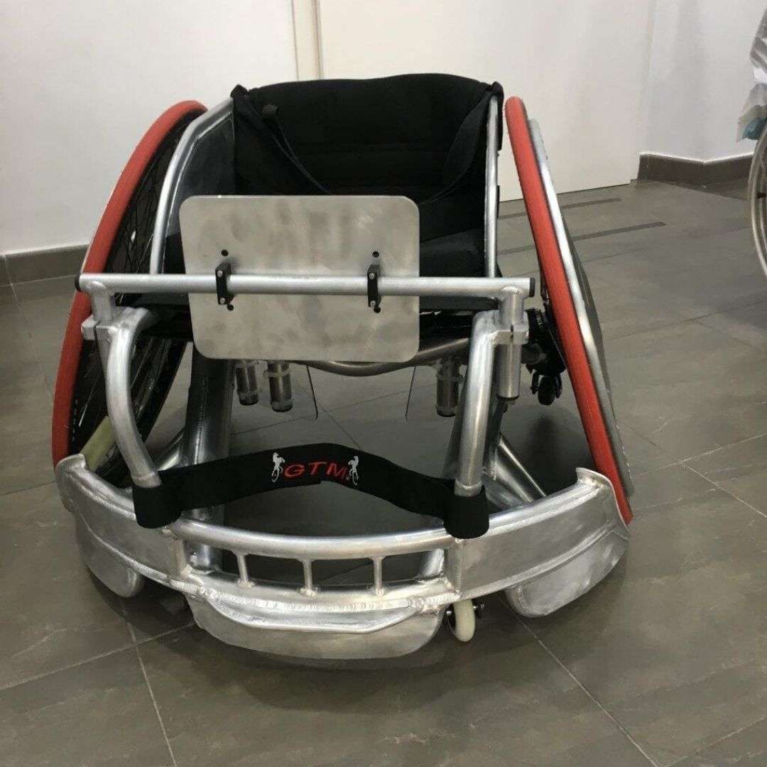 Una silla de ruedas plateada con ruedas rojas está sentada sobre un suelo de baldosas.