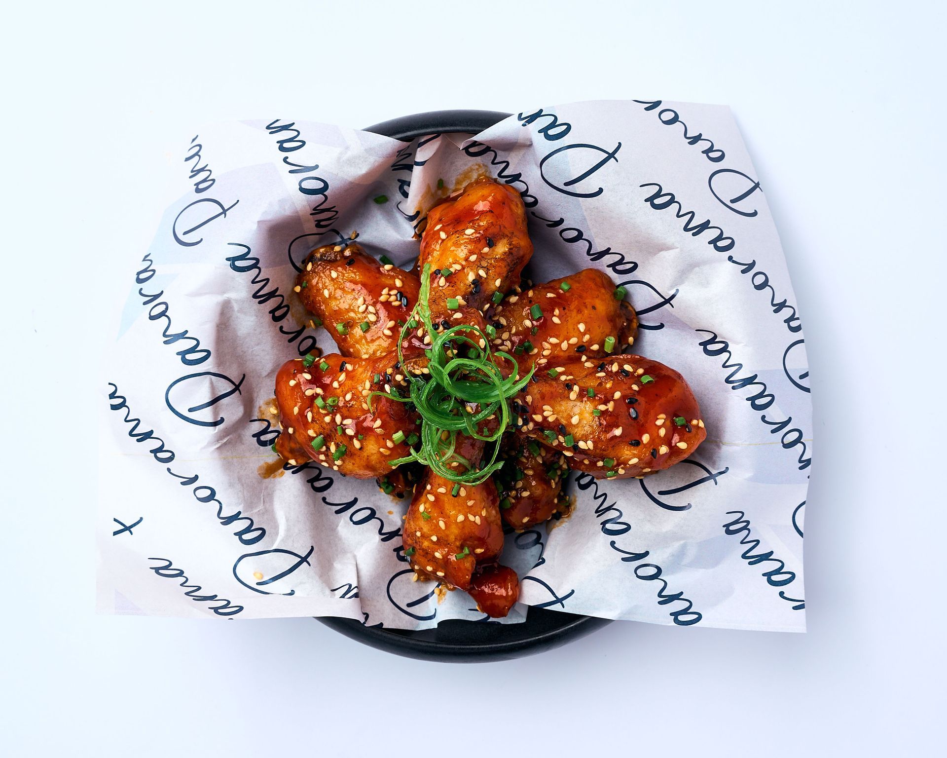 Un plato blanco cubierto con alitas de pollo y salsa sobre una mesa.