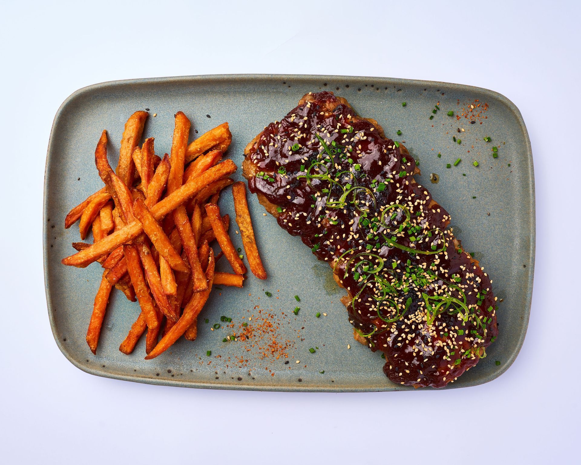 Un plato de costillas y patatas fritas de boniato sobre una mesa
