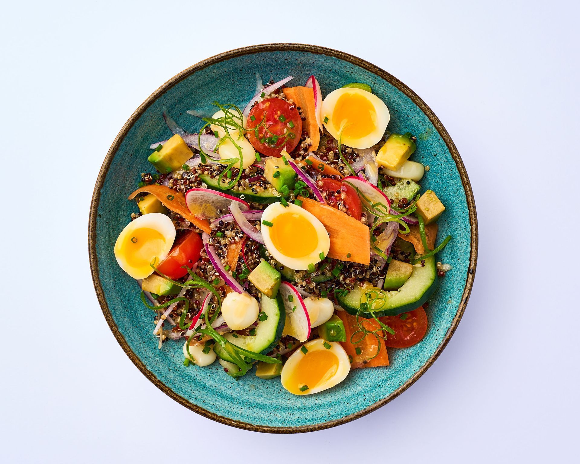 Una ensalada con huevos, zanahorias, tomates y rábanos en un plato azul sobre una mesa.
