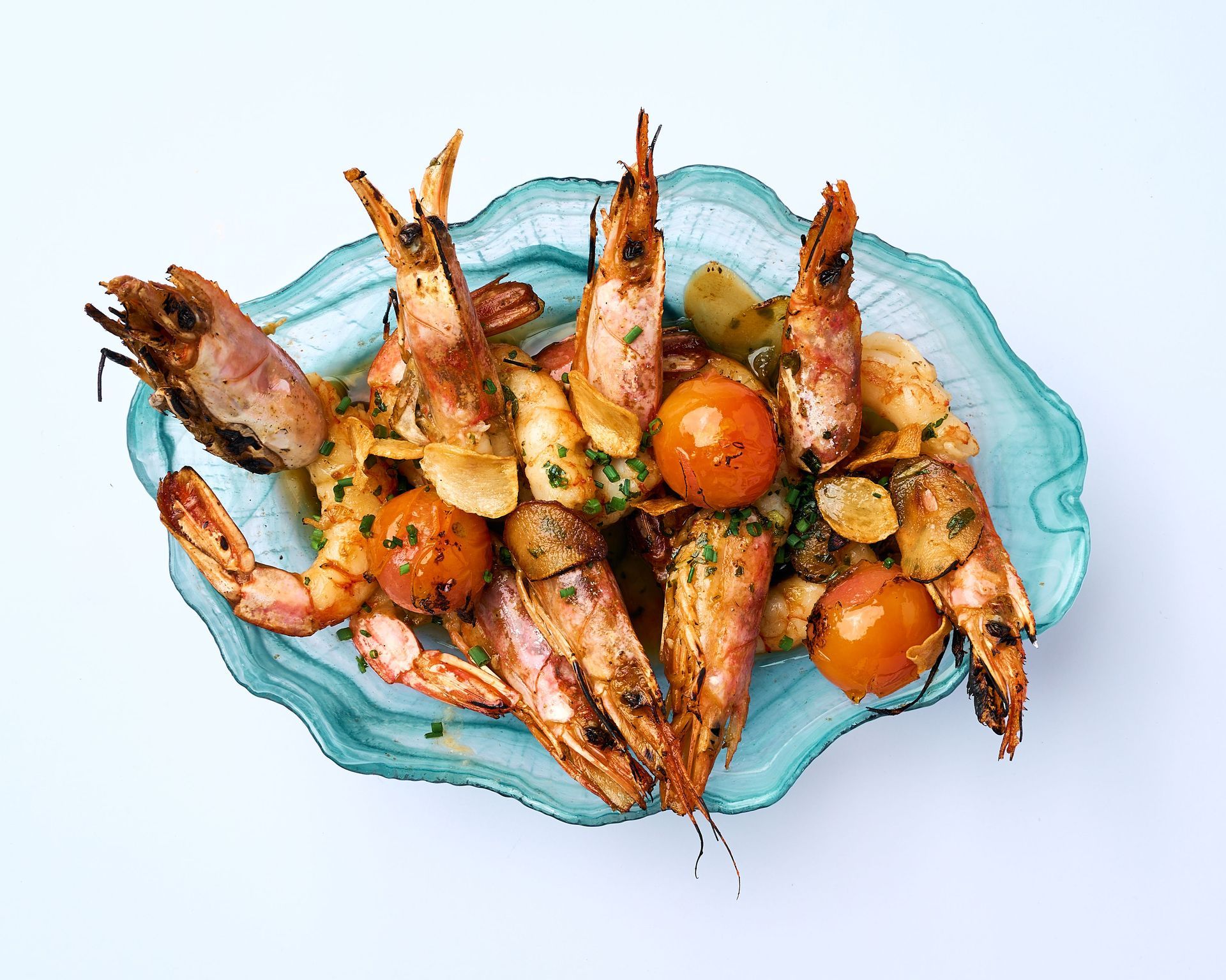 Camarones a la parrilla con tomates y cilantro en un plato de vidrio azul sobre una superficie de madera.