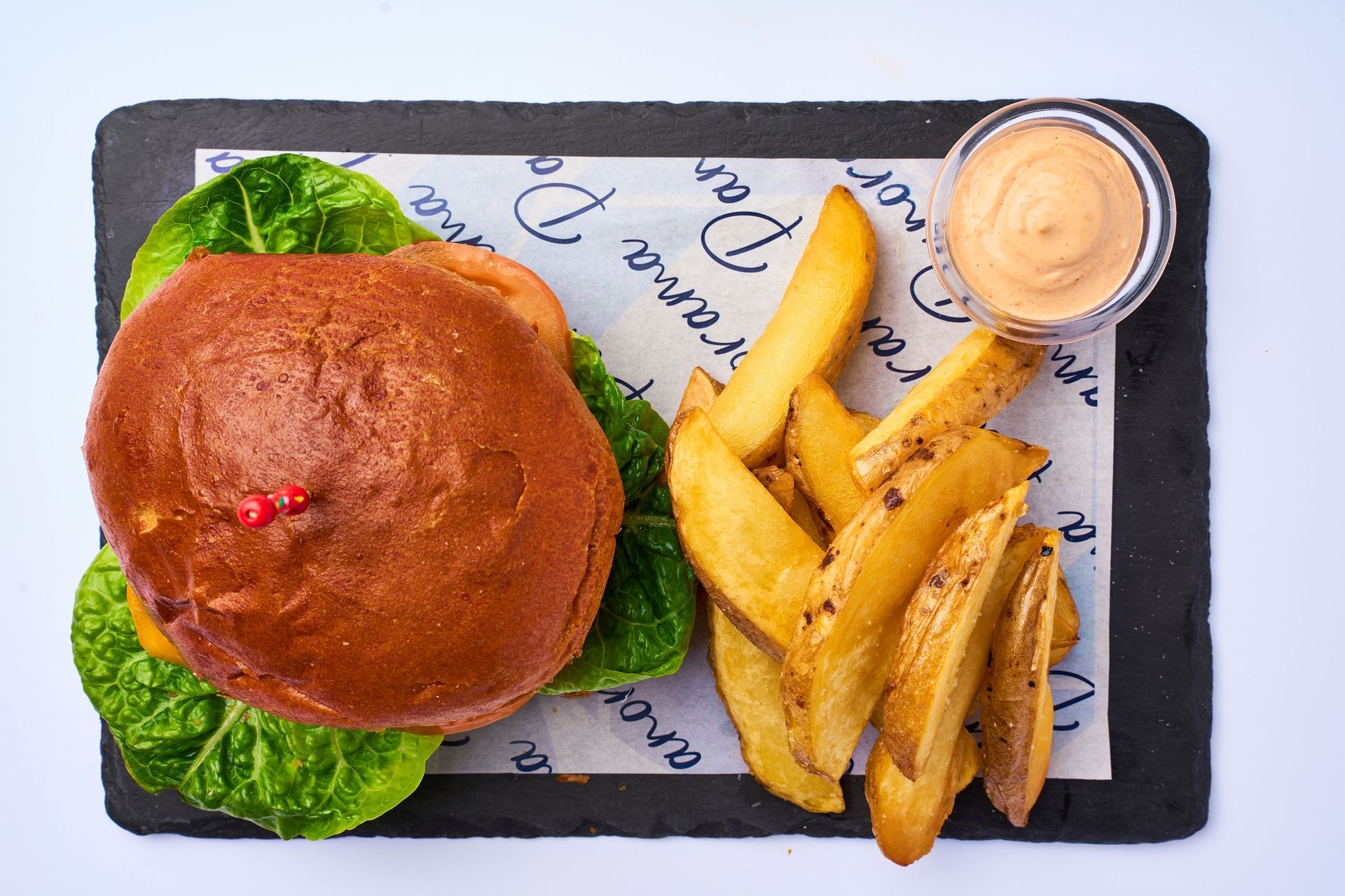 Una hamburguesa y papas fritas están sobre un periódico sobre una tabla de cortar.