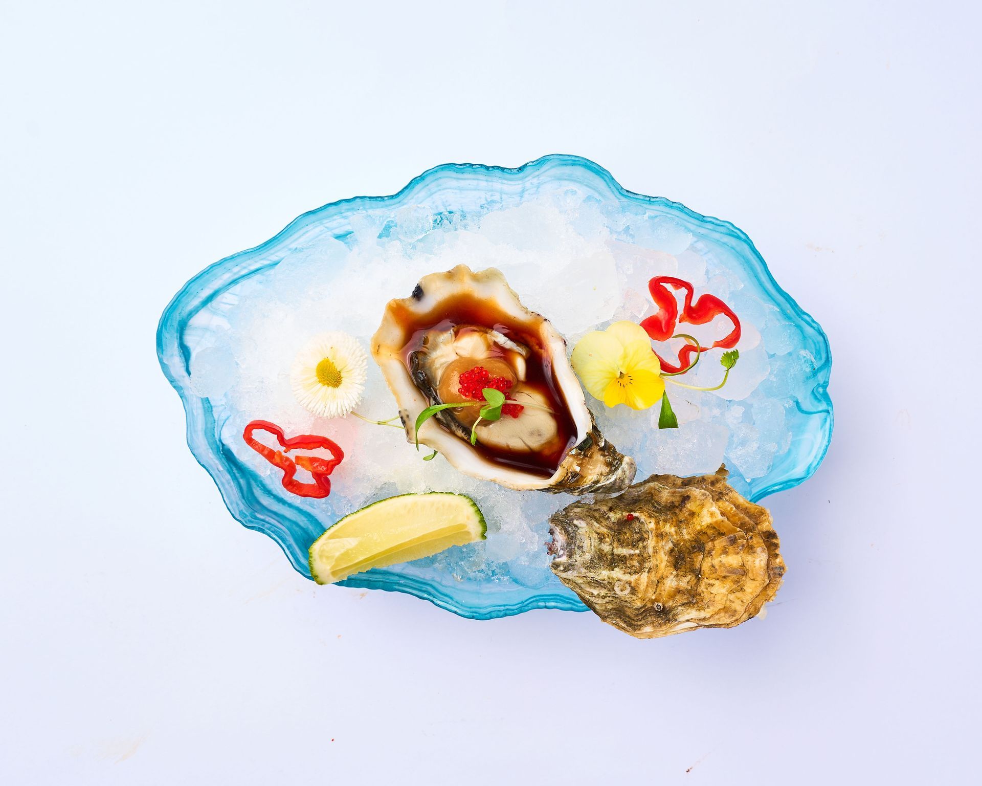 Un plato de ostras en hielo con salsa encima.