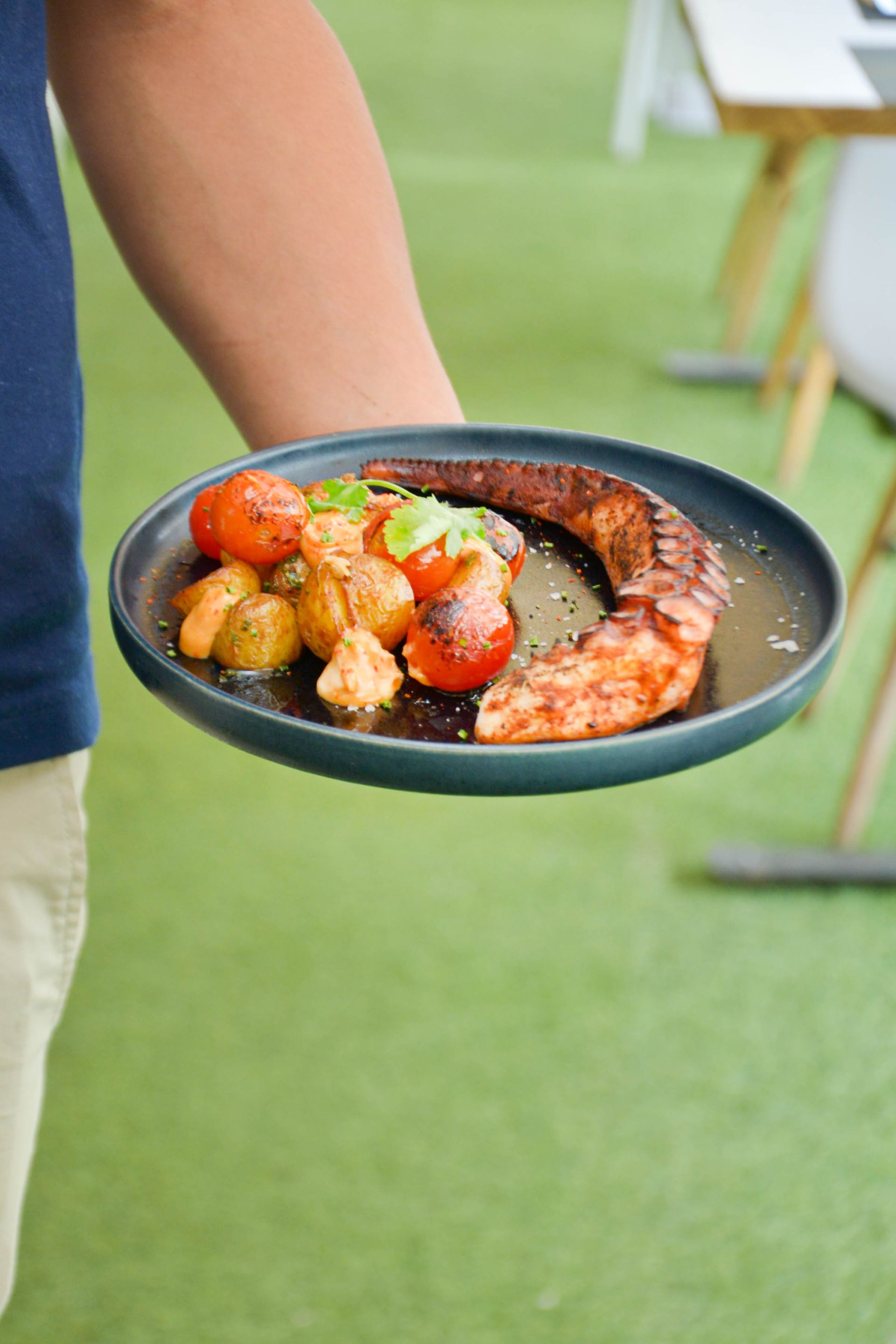 Una mesa cubierta de ostras y rodajas de limón con gente sentada en mesas al fondo.