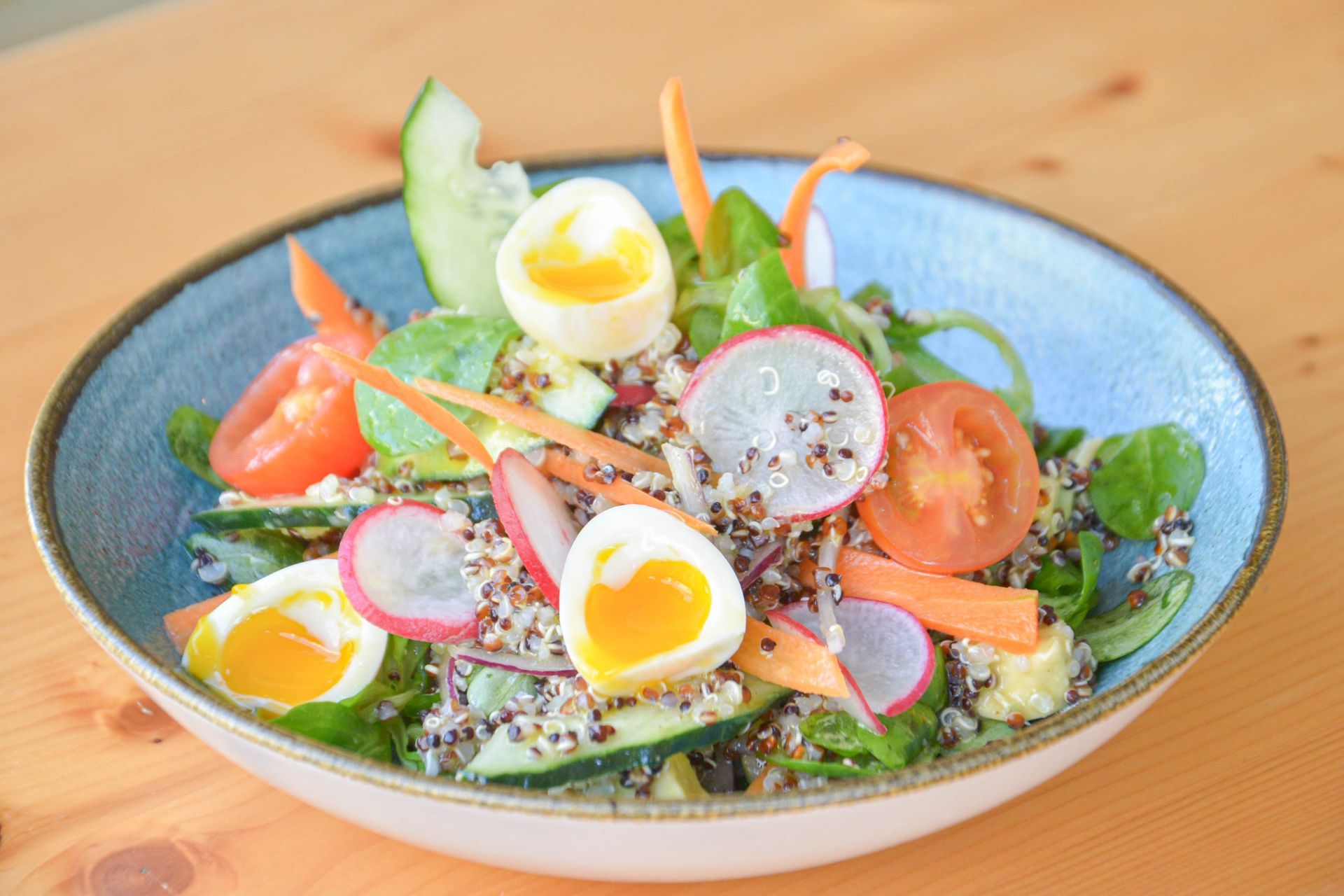 Una ensalada con huevos, zanahorias, tomates y rábanos en un plato azul sobre una mesa.