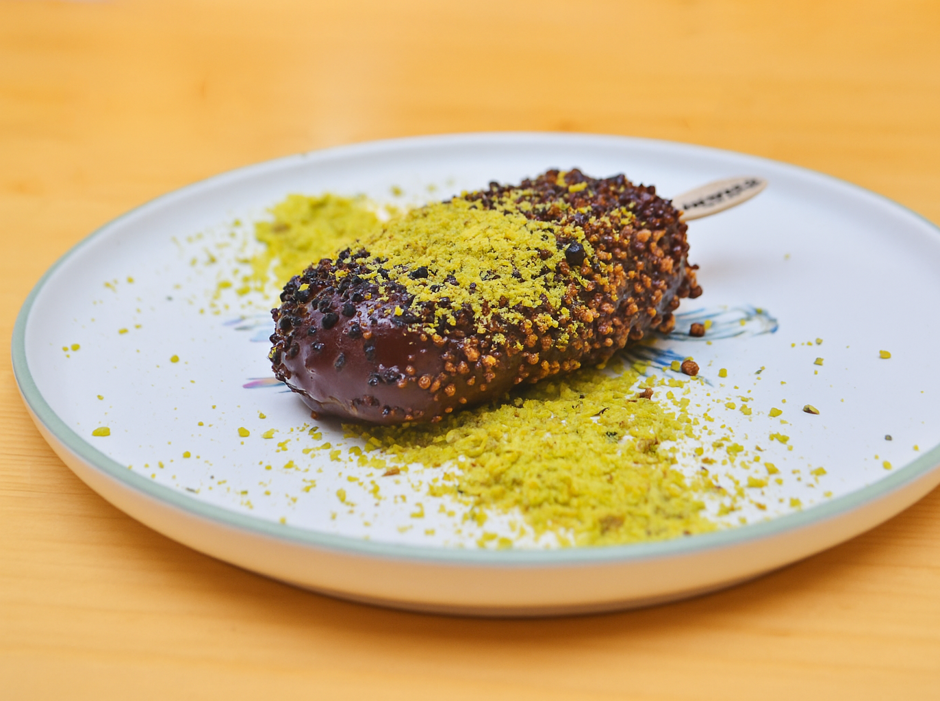 Un plato blanco cubierto con una barra de helado de chocolate sobre una mesa de madera.