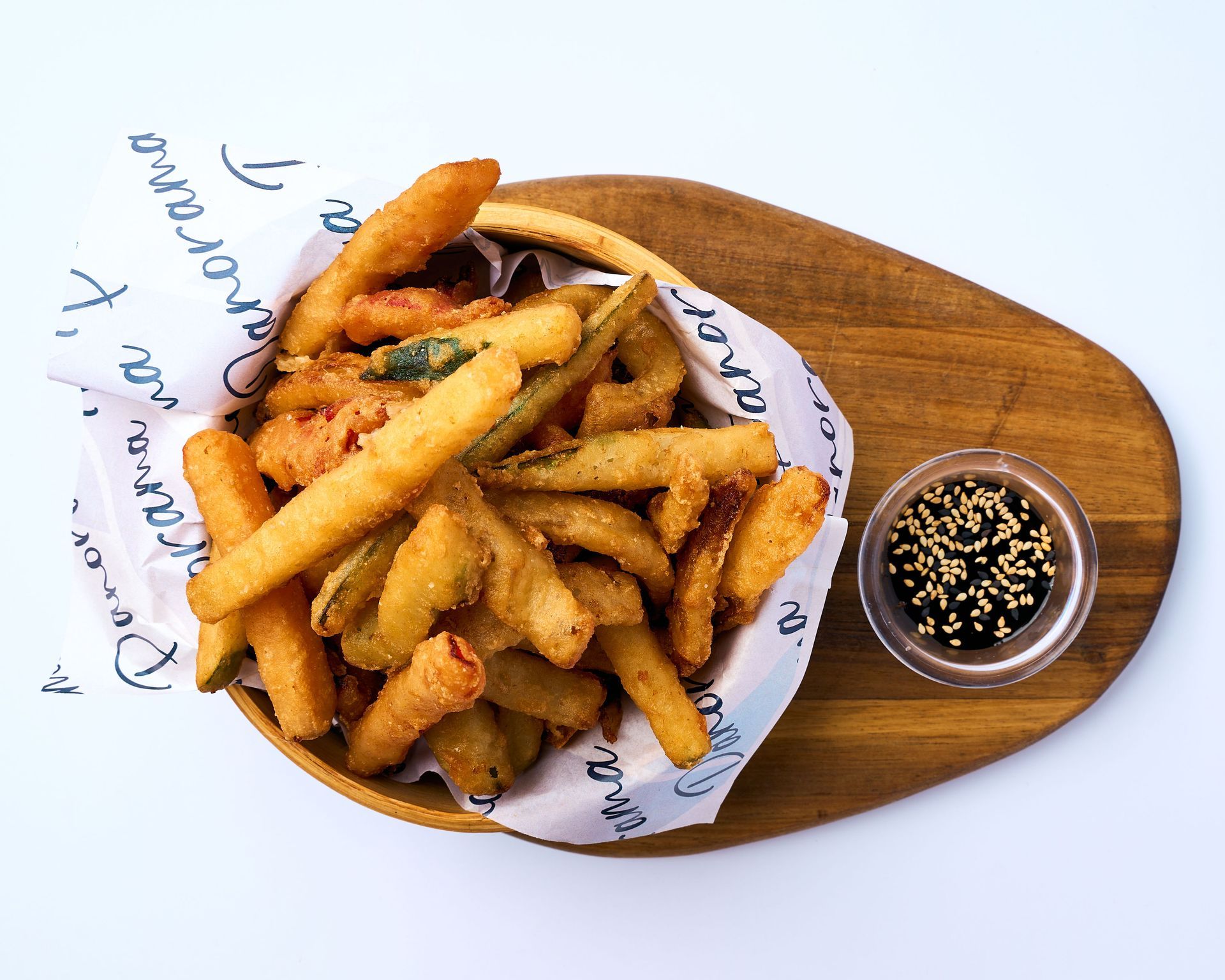 Un tazón de comida frita con un vaso de salsa para mojar sobre una tabla de cortar de madera.