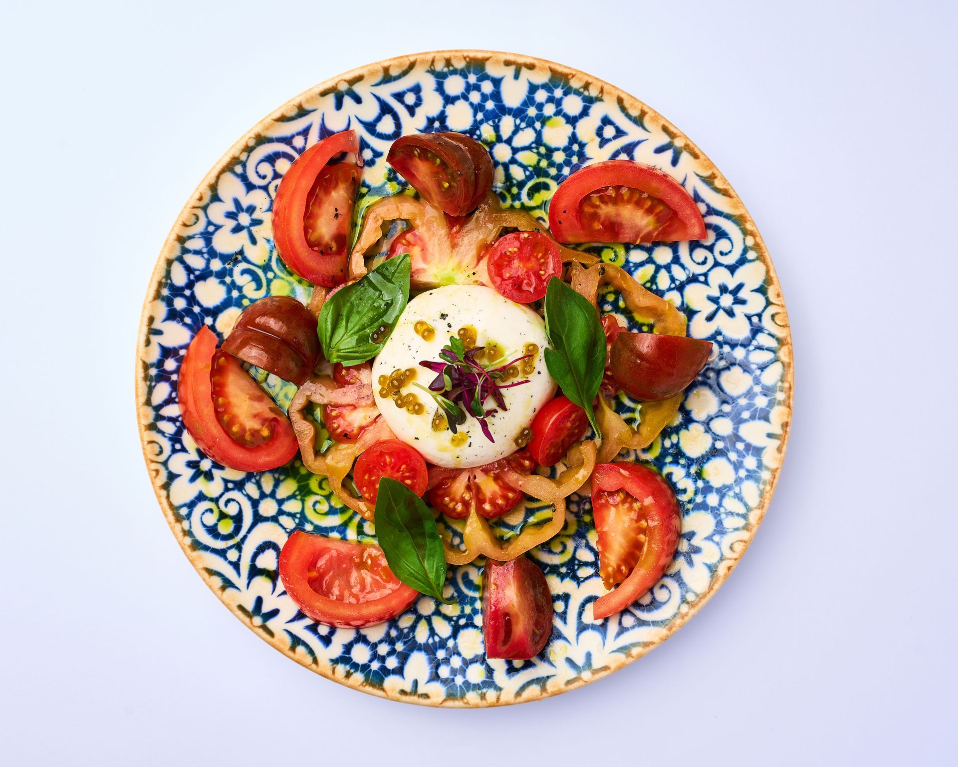 Un plato azul y blanco cubierto con tomates y queso mozzarella.