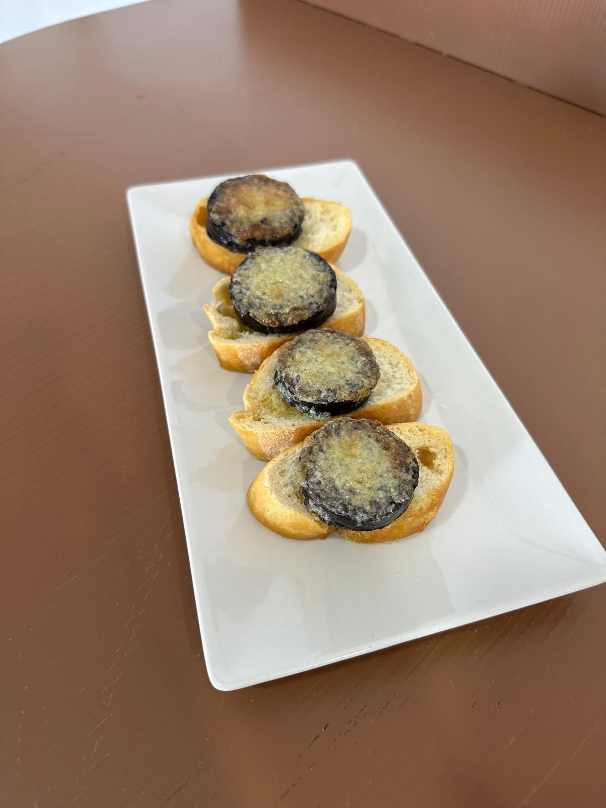 Rebanadas de pan cubiertas con comida oscura, redonda y cocinada sobre una bandeja rectangular blanca.