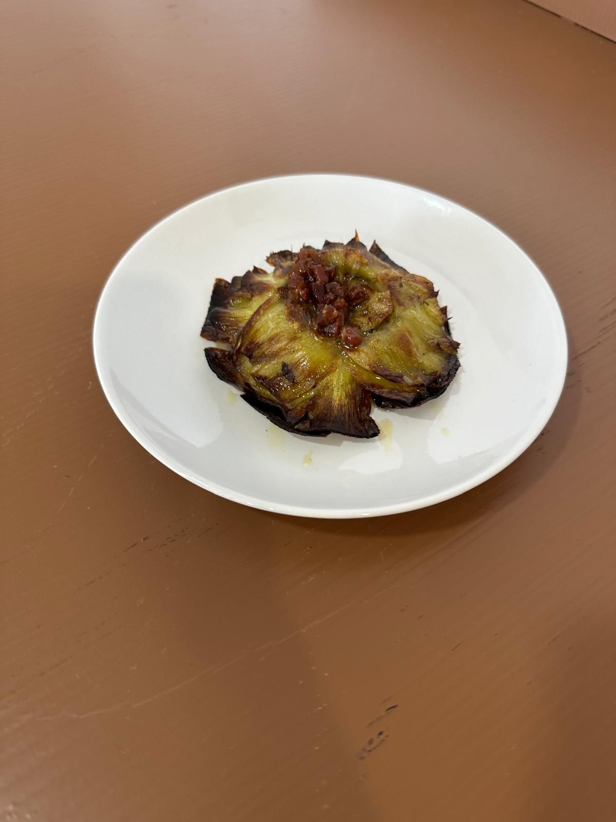 Corazón de alcachofa a la parrilla con aderezos sobre un plato blanco. Fondo de mesa marrón.