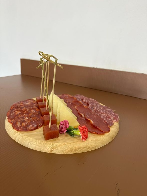 Tabla de embutidos con carnes en lonchas, queso y dulce de membrillo sobre una superficie de madera.