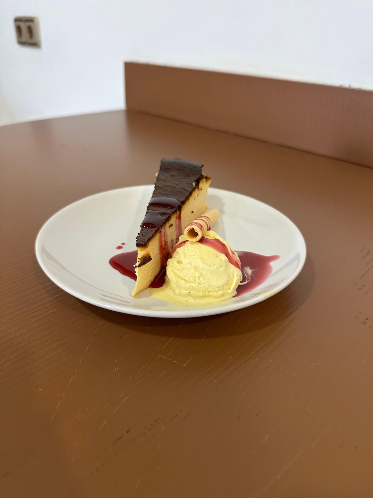 Rebanada de pastel con glaseado de chocolate, helado y salsa en un plato blanco.