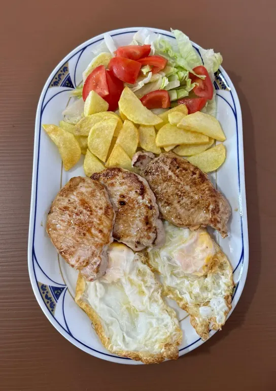 Plato de comida con carne a la parrilla, huevos fritos, patatas fritas y ensalada.
