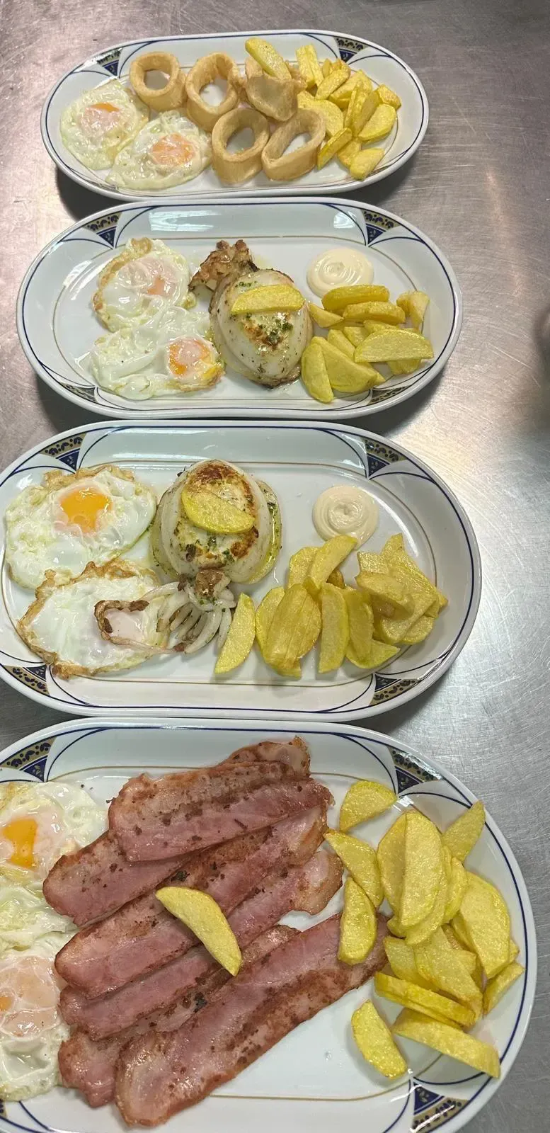 Cuatro platos de comida: huevos fritos, tocino, calamares y papas fritas en gajos.