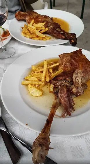 Dos platos de carne asada con papas fritas. Uno con un hueso desprendido. Mesa preparada.