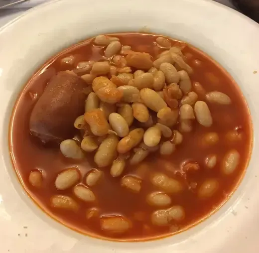 Plato de judías blancas en salsa roja con trozo de chorizo.