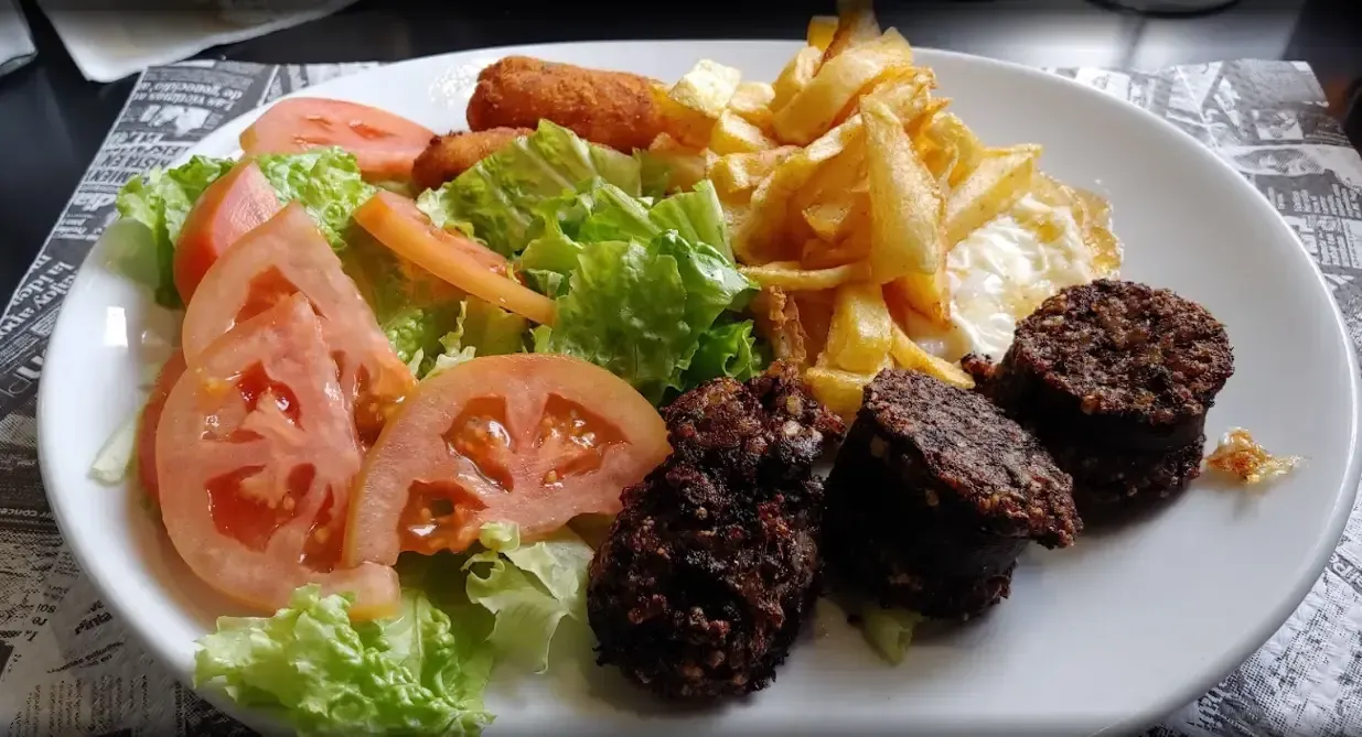 Plato con ensalada, patatas fritas, salchicha frita y palitos empanizados.