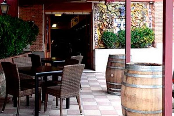 Zona de estar al aire libre con mesas y sillas cerca de la entrada de un restaurante con barriles decorativos y una pared de mosaico.