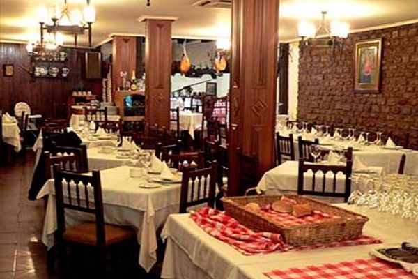 Interior de restaurante con mesas preparadas para comer, columnas y paneles de madera oscura.