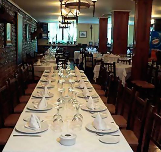 Mesa de comedor larga dispuesta para comer en un restaurante con mantelería y vasos blancos.