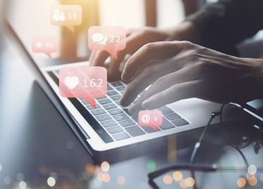 Persona escribiendo en una computadora portátil, notificaciones de redes sociales con corazones, burbujas de comentarios e íconos de seguidores superpuestos.