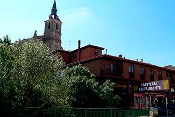 Campanario de una iglesia detrás de un edificio de ladrillos rojos con un cartel de 