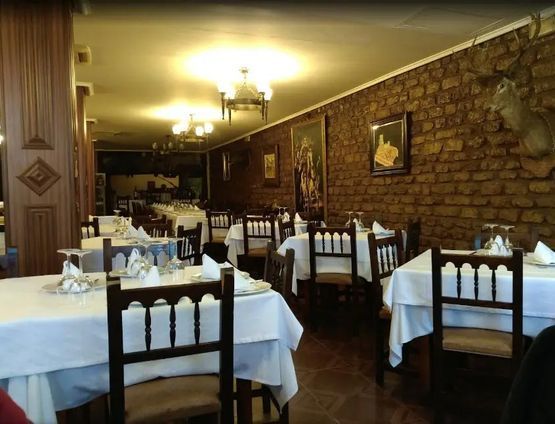 Interior de restaurante con manteles blancos, sillas de madera, pared de ladrillo e iluminación ornamentada.