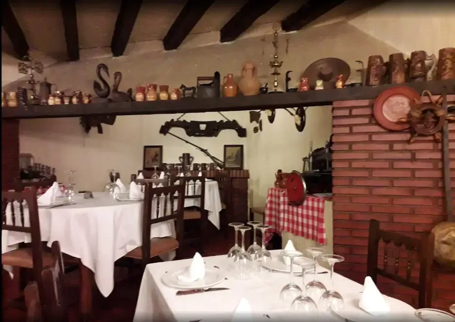 Interior de restaurante con manteles blancos, sillas de madera, pared de ladrillo y elementos decorativos.
