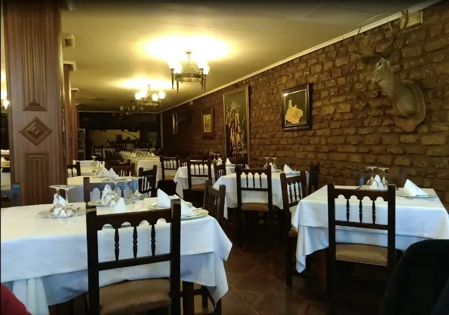 Interior de restaurante con manteles blancos, pared de ladrillo y montura de cabeza de ciervo.
