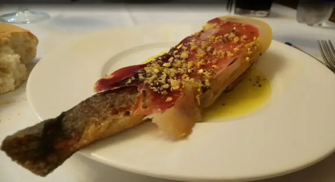 Pan cubierto con jamón y nueces sobre un plato blanco con aceite.
