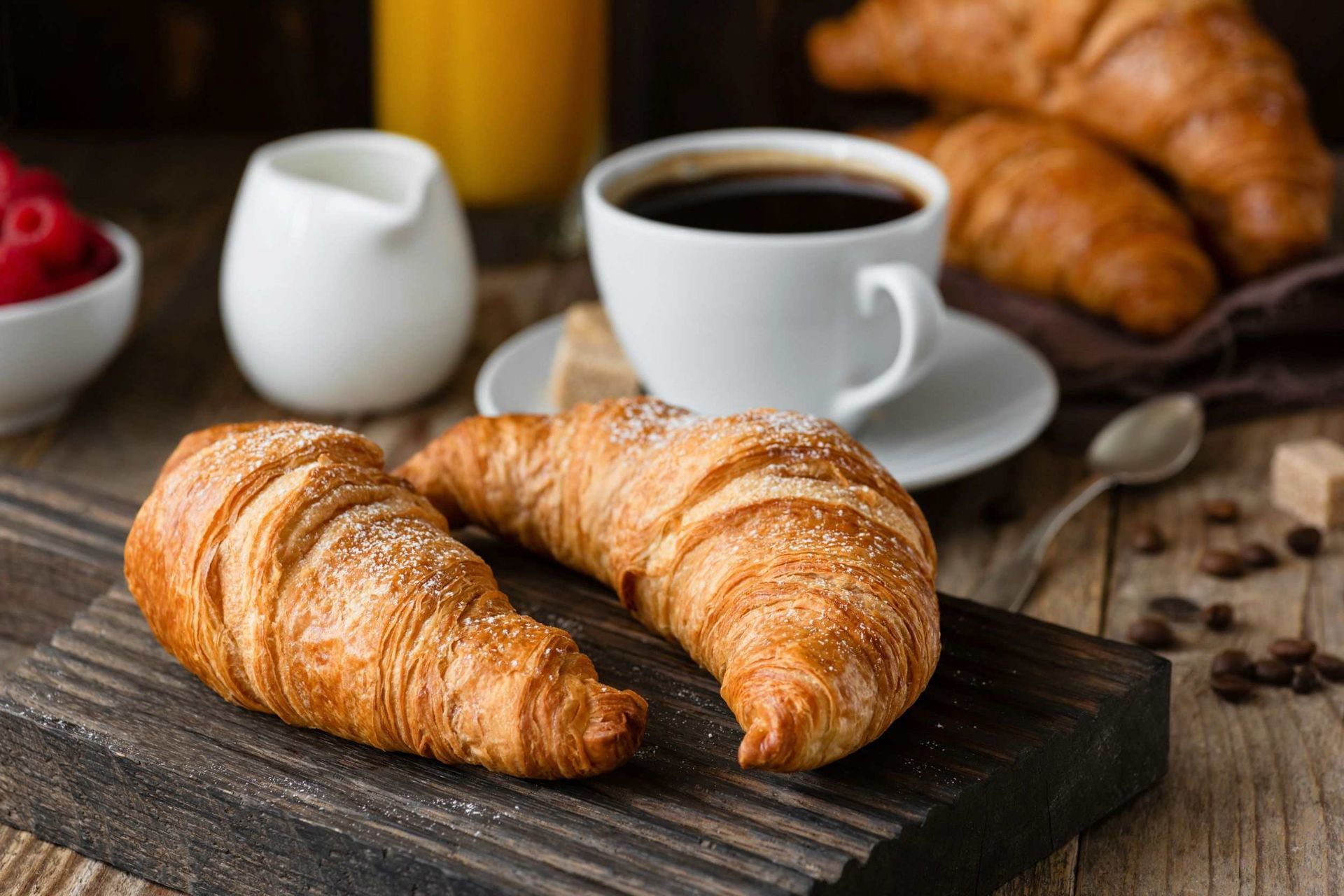 Hay dos croissants sobre una tabla de cortar de madera al lado de una taza de café.