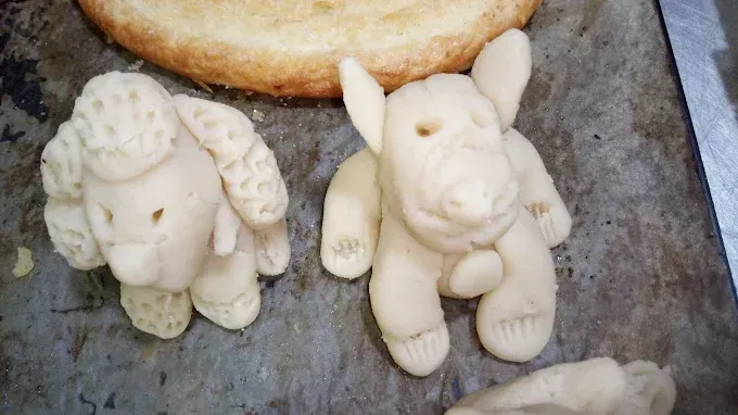 Dos animales hechos de masa están sentados en una bandeja al lado de un trozo de pan.
