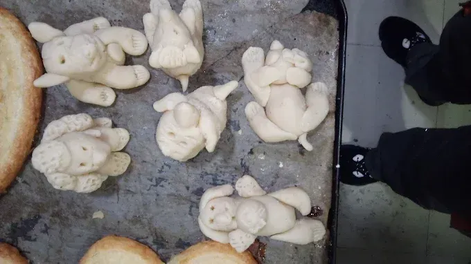 Una persona está de pie junto a una bandeja de pan con animales hechos de masa.