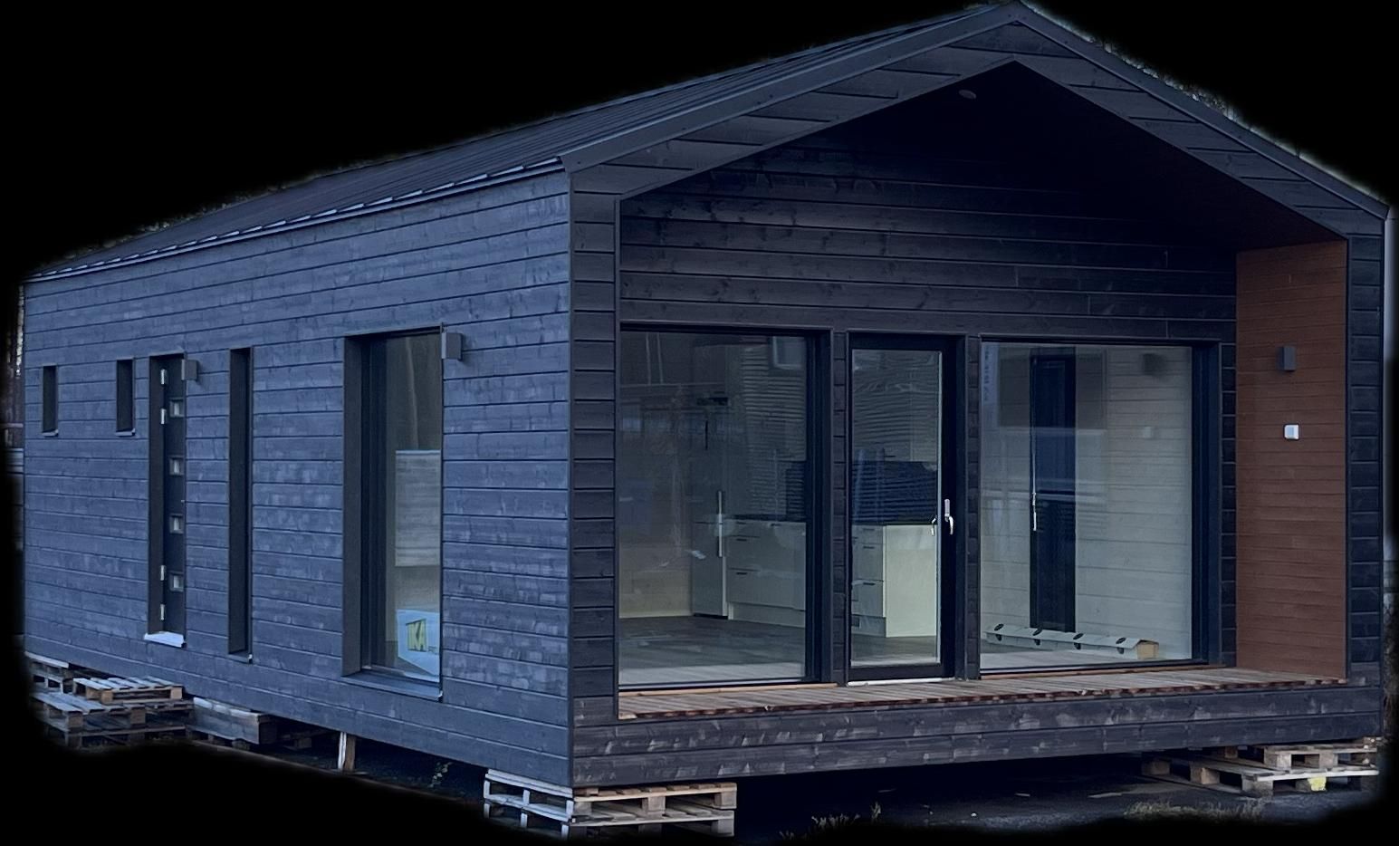 Tummansininen moderni pieni koti, jossa on suuret lasiovet ja -ikkunat, puinen ulkoverhous ja harjakatto.