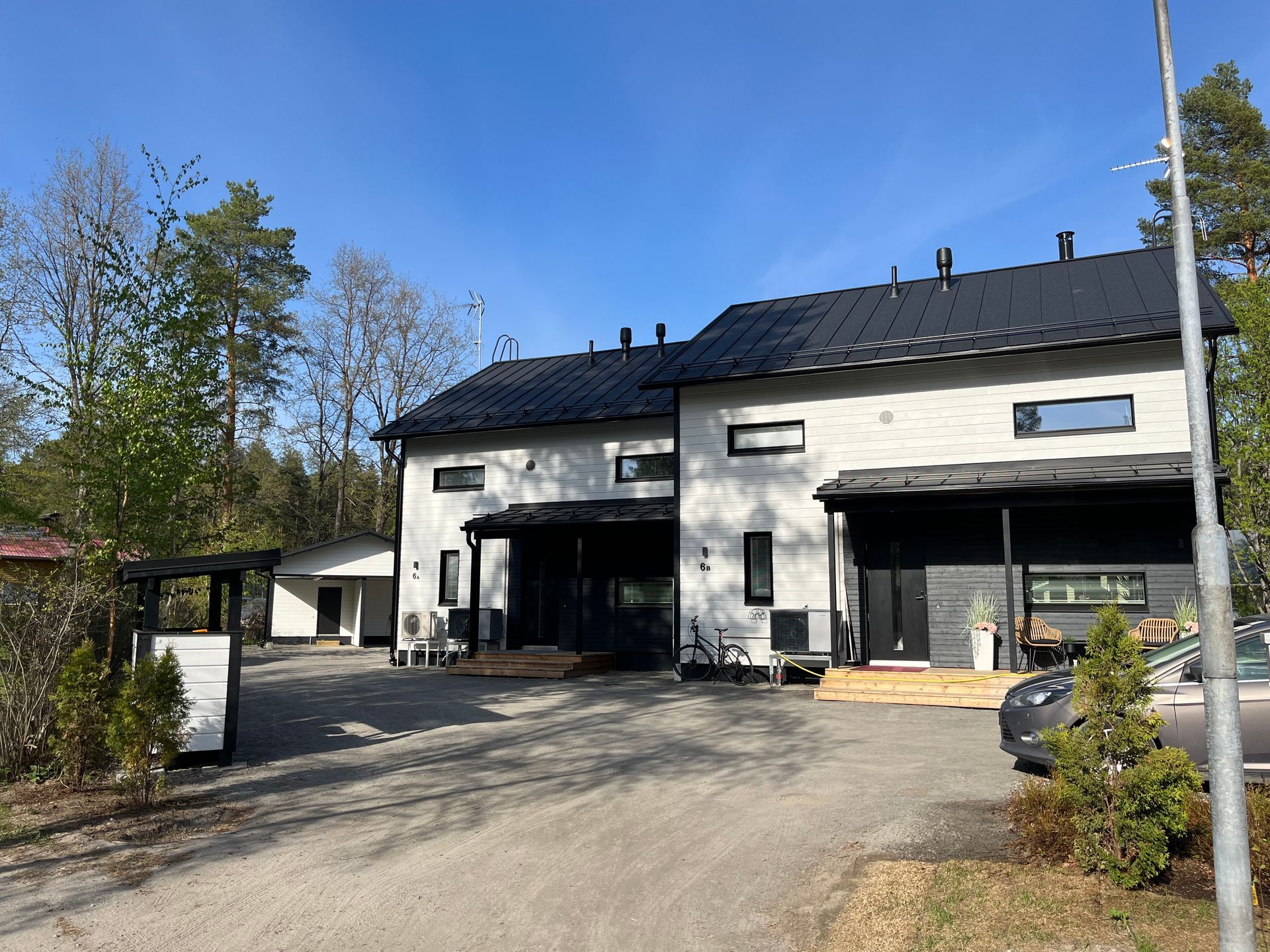 Kaksikerroksisia moderneja koteja mustilla katoilla, tummilla etukuisteilla ja vaalealla ulkoverhouksella aurinkoisena päivänä.