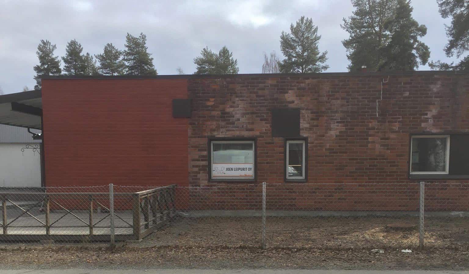 Punatiilirakennus, jossa on pienet ikkunat, aita ja taustalla paljaita puita.