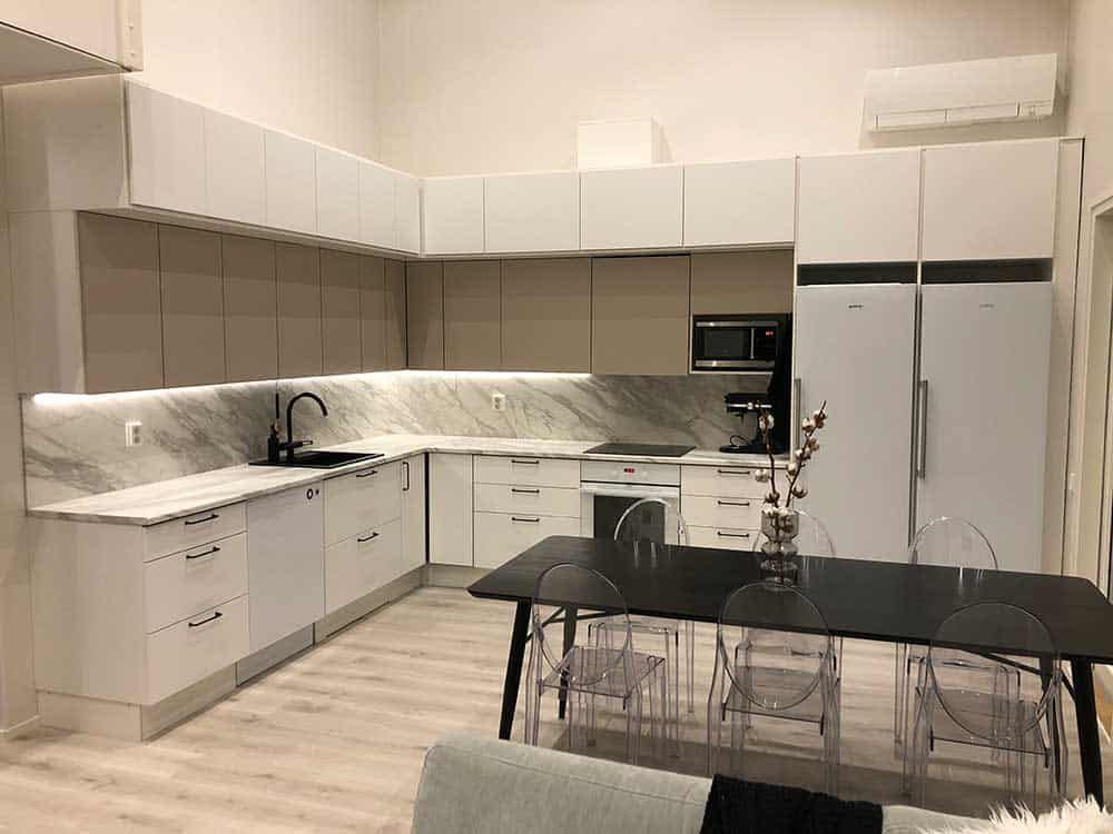 Moderni valkoinen keittiö, jossa marmoritasot, musta pöytä ja läpinäkyvät tuolit.