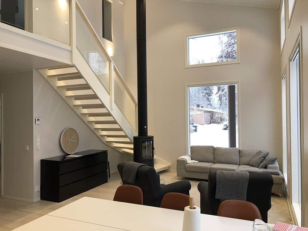 Olohuone, jossa portaikko, takka ja sohva, ikkunoista on näkymät lumiseen maisemaan.