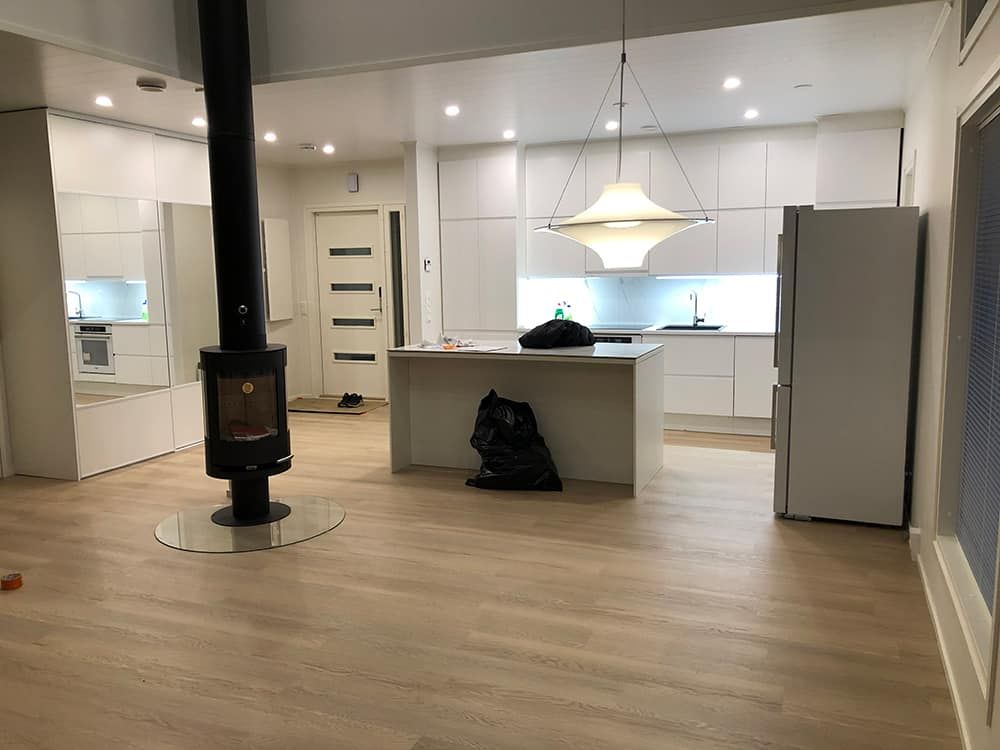 Moderni keittiö, jossa valkoiset kaapistot, saareke, vaaleat puulattiat ja musta liesi.