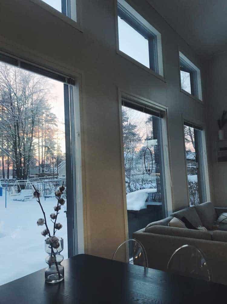 Luminen näkymä suurista ikkunoista, kukkamaljakko pöydällä valoisassa olohuoneessa.