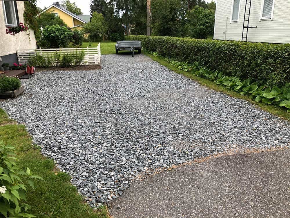 Soratie pienellä peräkärryllä. Talo ja vihreät pensaat reunustavat harmaita kiviä.